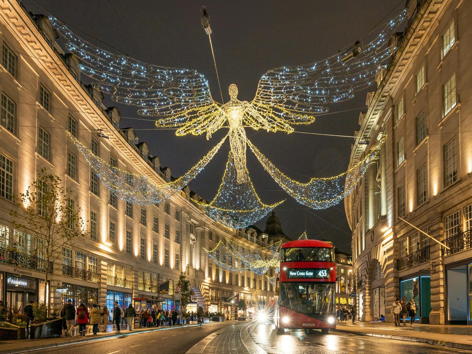 Stunning evening view of Regent Street in London, adorned with festive angel lights and iconic red double-decker bus.