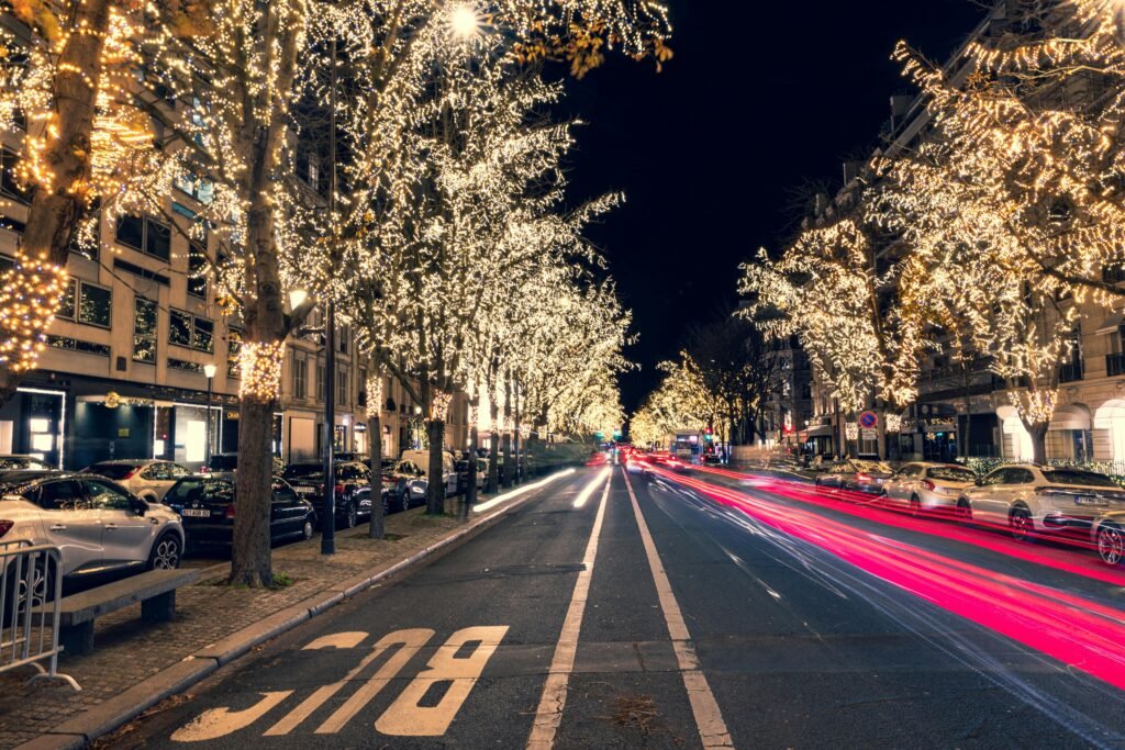 A beautifully lit street in Paris, France during the holiday season with festive lights and bustling traffic.